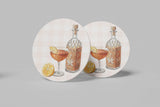 a round coaster with a cocktail glass and a bottle of alcohol, along with slices of orange and lemon.