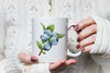 a woman holding a coffee mug with blue berries on it