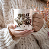 a woman holding a coffee mug with a picture of two women on it