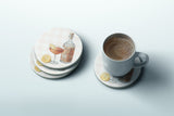 a set of coasters with illustrations of a cocktail glass, lemon slices, and a bottle of liquor, along with a cup of coffee on a matching coaster.