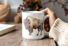 a person holding a coffee mug with a picture of a bison on it