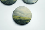 three oval paintings of a field of grass