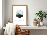 a framed poster of a city skyline with the word "Bellingham" written on it, placed on a shelf next to a wicker chair and a plant.