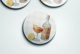 A round coaster with an illustration of a cocktail glass, a bottle, and lemon slices.