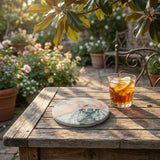 Artistic close-up of a single sandstone coaster revealing detailed botanical design and natural texture against a blurred garden background.
