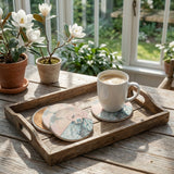 Full set of four sandstone coasters with botanical illustrations, arranged on a vintage wooden tray in a sunlit Southern-inspired sunroom.